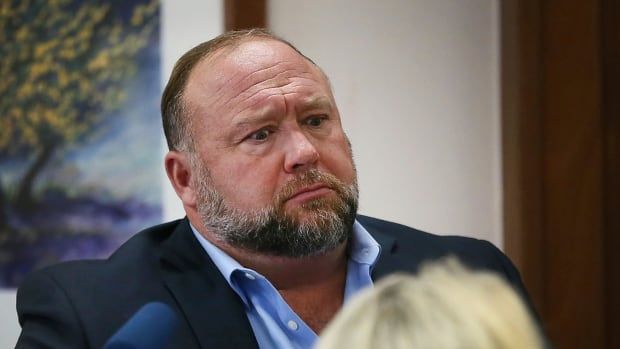 An overweight man with a beard sits in witness stand in a courtroom.