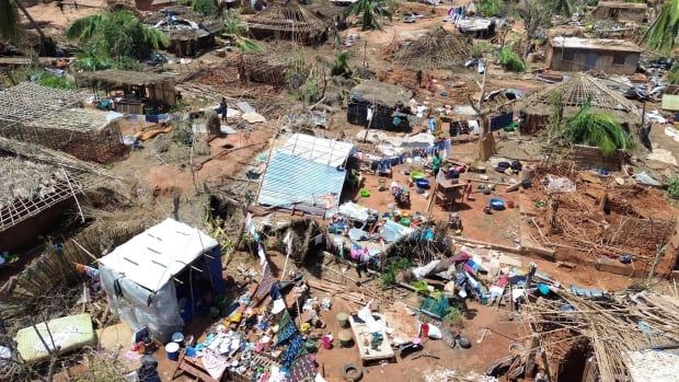 People stand amid destroyed buildings, uprooted trees and debris.