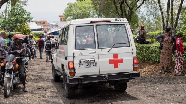 An ambulance drives down a road as people gather to the side.