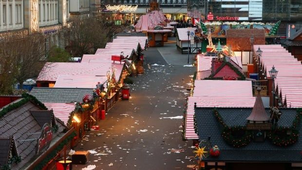 Closed Christmas market stalls with red and white striped roofs are lined on either side of a concrete pedestrian path, with trash on the ground.