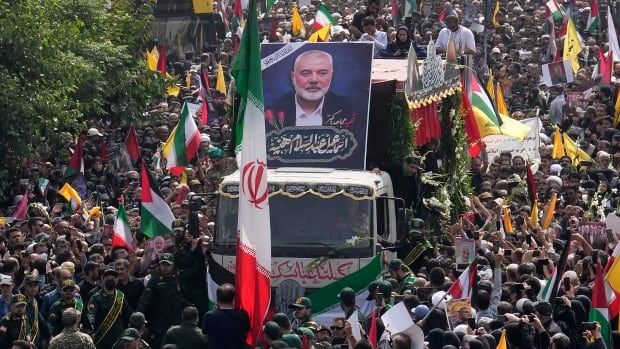 A truck with a banner depicting a man's face on top moves through a sea of people. The street is packed with people, all walking around the truck in the same direction.