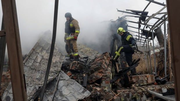 Two firefighters stand on a large pile of rubble.