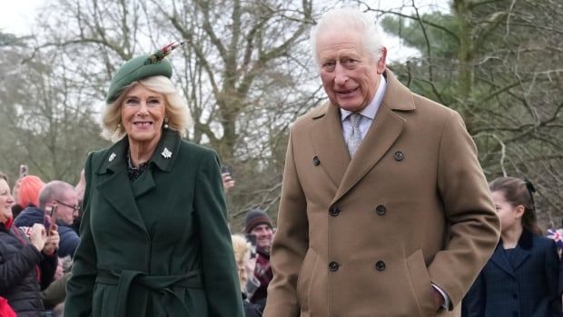 A woman in a green coat and hat and a man in a tan-coloured coat walk side by side.