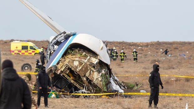 Police tape encircles the wreckage of an airplane as police officers stand guard.