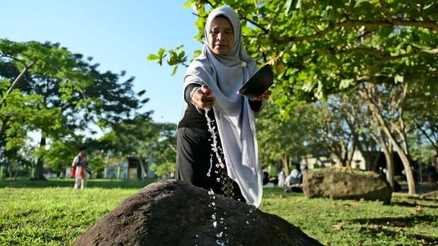 A woman sprinkles water on a stone marking a mass grave.