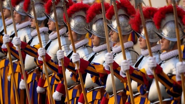 A line of guards in bright coloured uniforms and armour holding spears. 