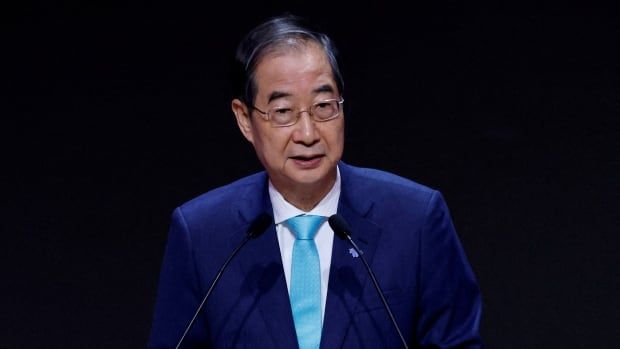 A man wearing a blue tie and suit delivers a speech from a podium.