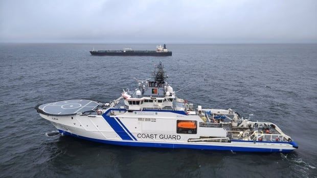 A coast guard boat is seen the foreground as an oil tanker is seen in the background.