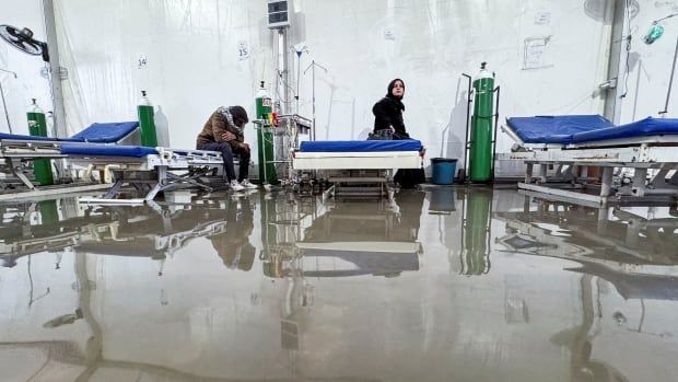 People sit in a flooded field hospital.