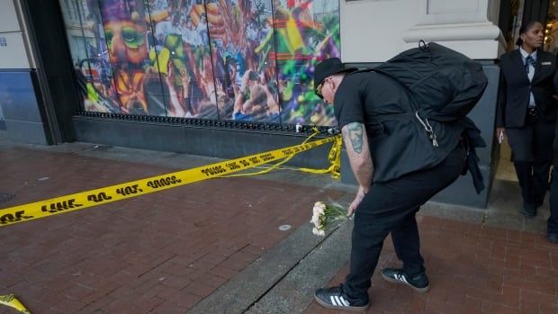 A man places a bouquet of flowers on the sidewalk.