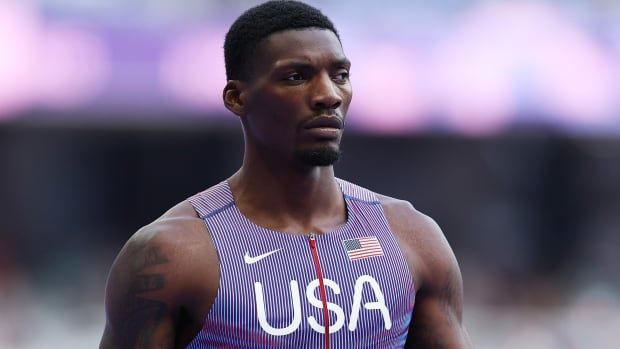 A male Olympic sprinter stands on the track during the day.