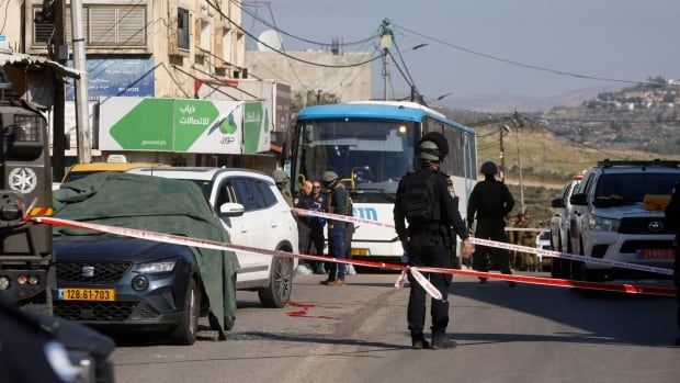 Tape is stretched across a road, with several vehicles and helmeted officers shown behind the tape. One of the vehicles is a bus.