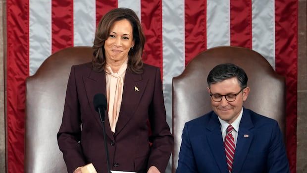 A woman stands while holding a gavel beside a man who is seated.