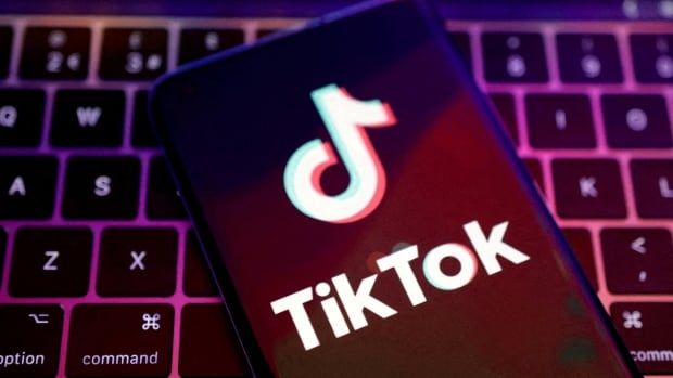 The app logo of TikTok is seen on a cellphone that is resting on a computer keyboard.