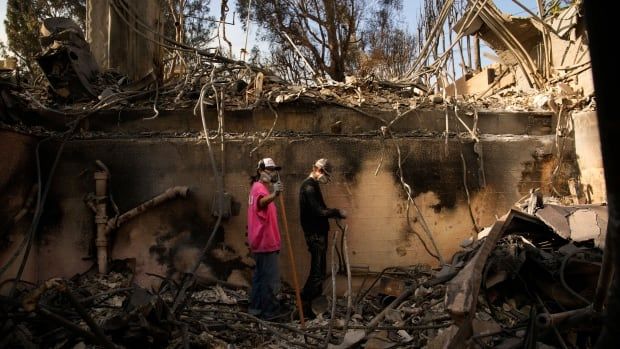 Two people pick through the rubble after a wildfire.