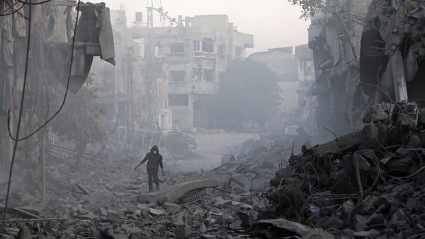 A person walks on rubble on a street lined with destroyed buildings.