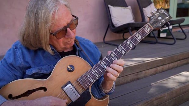 A man sits on the stairs outdoors and plays a guitary.