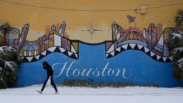 Person walk by a sign that reads Houston, on a street blanketed by snow.