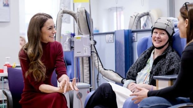 A person in a hospital talks with another person who is receiving intravenous treatment while another person looks on.