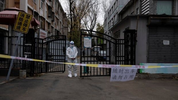 A person in a hazmat suit stands by gates of a residential building.