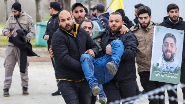 People carry an injured person in a street.