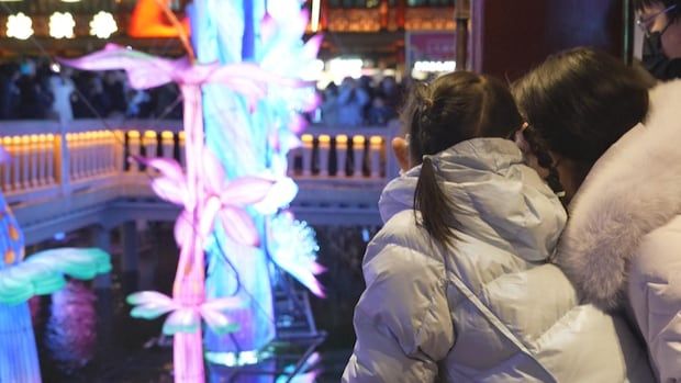 A mother and daughter watch a vivid paper flower lantern glowing blue and pink and purple.