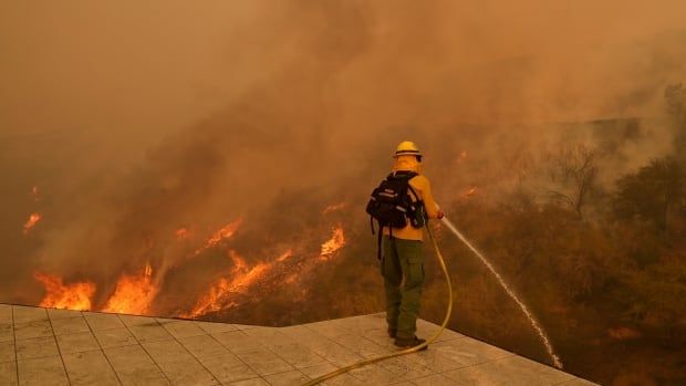 A firefighter hoses down flames as the Palisades Fire approaches in Mandeville Canyon, Jan. 11, 2025, in Los Angeles.