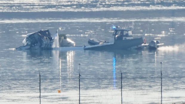 A small boat is shown in a body of water, near to fusillage wreckage.