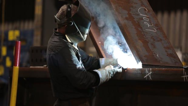 A masked worker welds a part at ADF Group's shop in Terrebonne, Quebec. The light from the welding aluminates the worker.