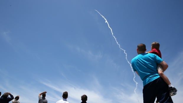 People look skyward at the trail left by a distant missile.