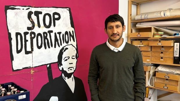 A man stands next to a poster that says 'Stop deportation.'