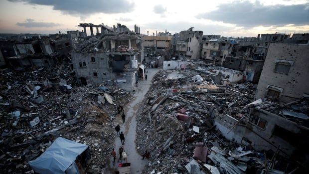 People walk next to rubble of destroyed buildings.