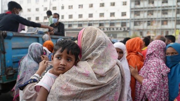 A woman holding a child waits queues with others in front of a blue truck handing out bags of food.