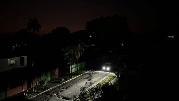 A car's headlight illuminates a street at night during a blackout.