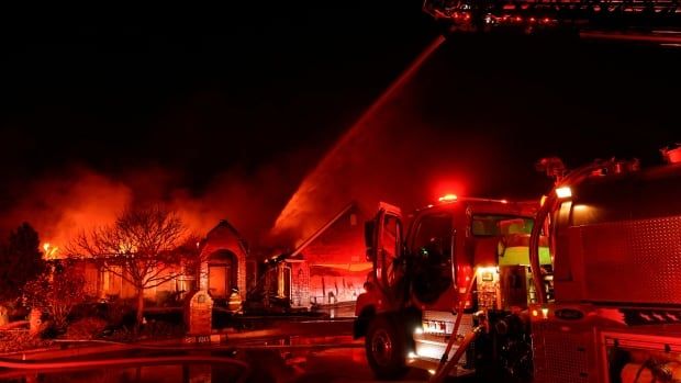 A firefighter sprays water on a house on fire, standing in front of a fire truck