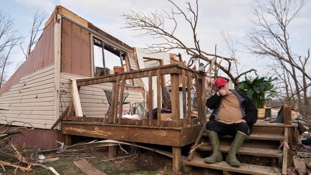 A person sits on the porch of a destroyed home.