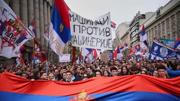 Protesters carry a large flag and hold up signs during a march.