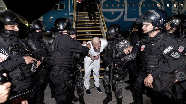 A handcuffed inmate is escorted by police off a plane.