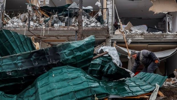 Man steps over what remains of his roof as he clears rubble left by a Russian drone strike.