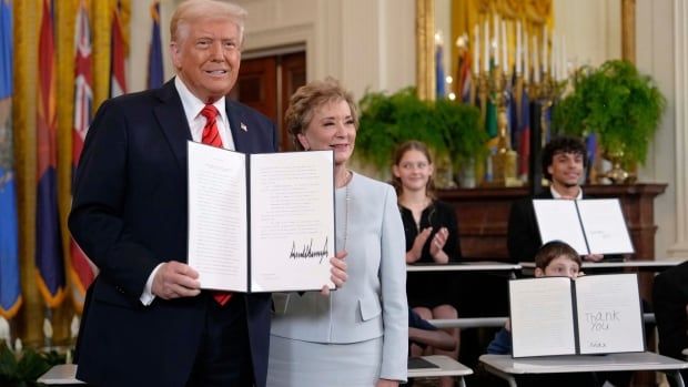 President Donald Trump holds up a signed executive order alongside Secretary of Education Linda McMahon