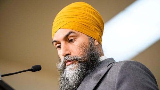 Jagmeet Singh stands at a podium looking down, he is wearing a grey jacket and a yellow turban