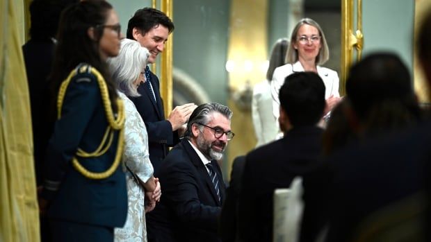 Clerk of the Privy Council John Hannaford participates in a signing, as Gov. Gen. Mary Simon and  Prime Minister Justin Trudeau look on. Hannaford is seated while the PM and GG stand behind him looking over his shoulder. 