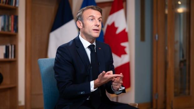 France’s President Emmanuel Macron sits in a chair wearing a blue suit as he is interviewed by CBC’s Chief Political Correspondent Rosemary Barton and Radio-Canada's Parliamentary Bureau Chief Louis Blouin who are off camera. 