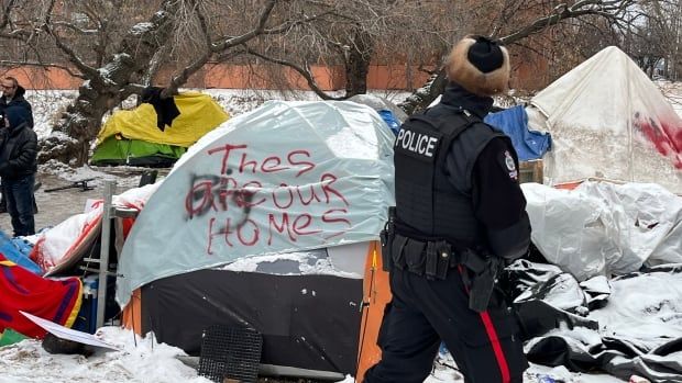 An Edmonton police officer passes in front of a tent that reads "These are our homes." 