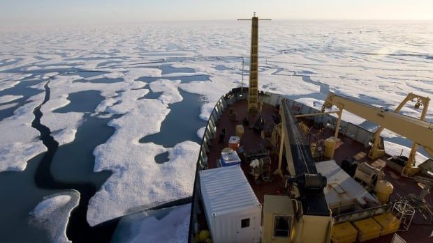 A photo taken from onboard a ship, looking down at its bow as it cuts through icy water.