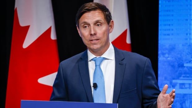 A man gestures with his hand as he speaks at a podium.