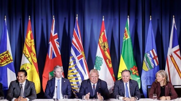 Five people sit at a table in front of flags.