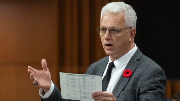 A politician speaks in a legislature. He's holding a piece of paper in one hand.