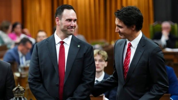 Three men in suits stand in a legislative chamber.