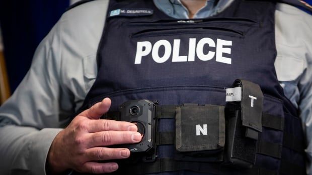 A police officer demonstrates and turns on a body camera that he's wearing on the front of his vest.